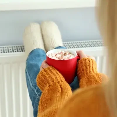 personne buvant une boisson chaude les pied sur le radiateur profitant du confort thermique de son logement à Arras